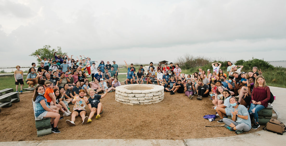 A group of a few dozen people all surrounding a campfire pit in rockport, texas.