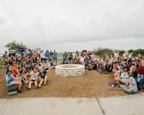 A group of a few dozen people all surrounding a campfire pit in rockport, texas.